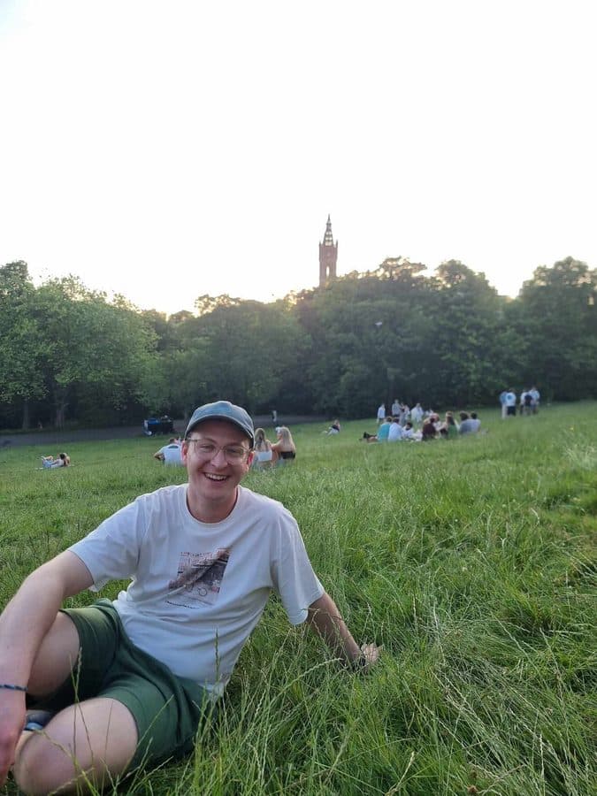 Aidan sitting in a grassy park at sunset